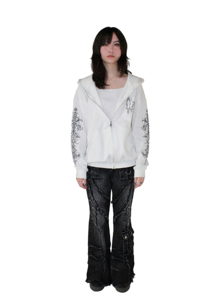 Person wearing a white hoodie with floral designs and black pants on a plain background