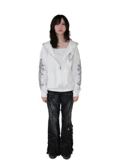 Person wearing a white hoodie with floral designs and black pants on a plain background