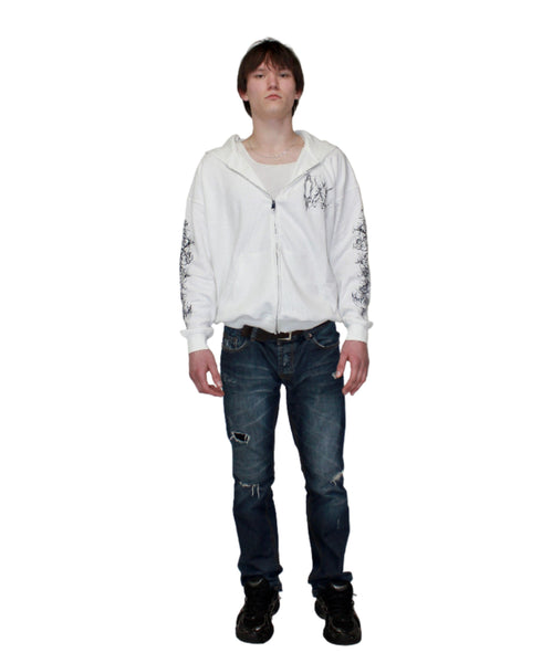 Person wearing a white hoodie with text and graphics, dark jeans, and black shoes on a plain background
