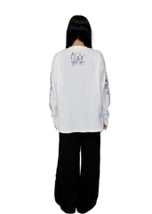 Person wearing a white long-sleeve shirt with black text and graphics on the back, standing against a plain white background.