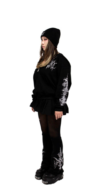 Person wearing a black outfit with white designs on sleeves and boots against a white background