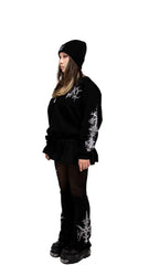 Person wearing a black outfit with white designs on sleeves and boots against a white background