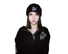 Person wearing a black hoodie and cap with white designs on a plain background