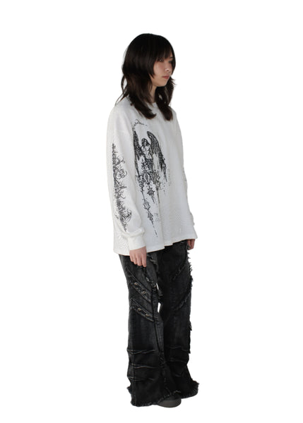 Person wearing a white shirt with black patterns and black pants on a plain background